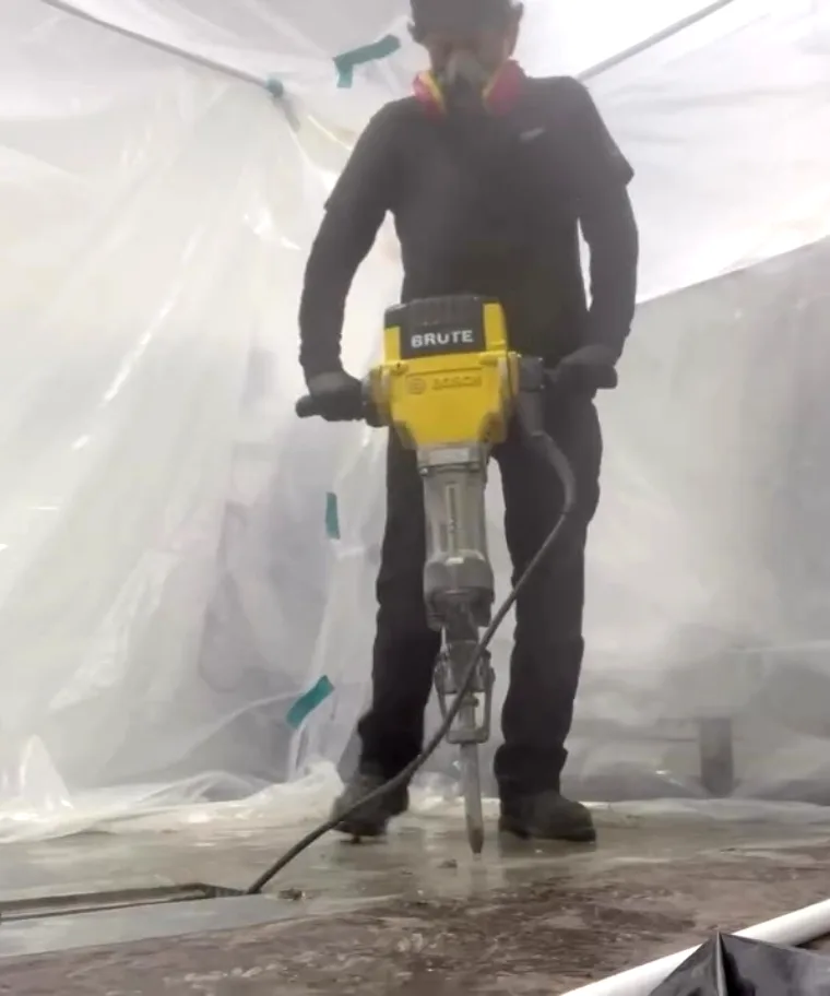 A technician breaking out a commercial kitchen floor inside a sealed plastic containment