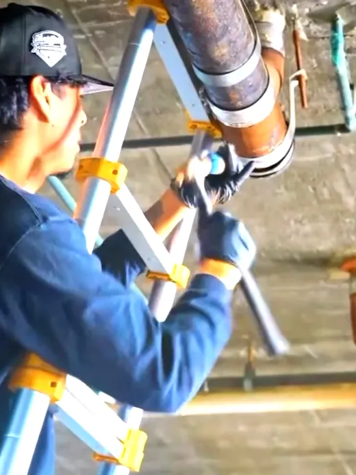 A technician on a step ladder working on overhead cast iron and copper waste lines