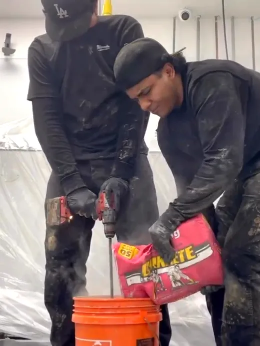 Two technicians mixing and pouring material into a bucket beside the opened floor