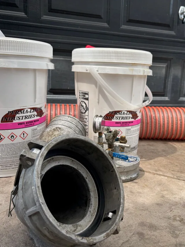 Two pails of Perma-Liner vinyl ester resin beside the liner tube and the inversion drum, set out before a lining run