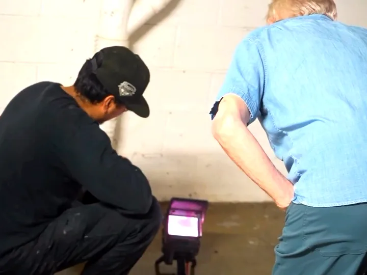 A technician crouched over an inspection monitor on the floor with the property owner watching alongside
